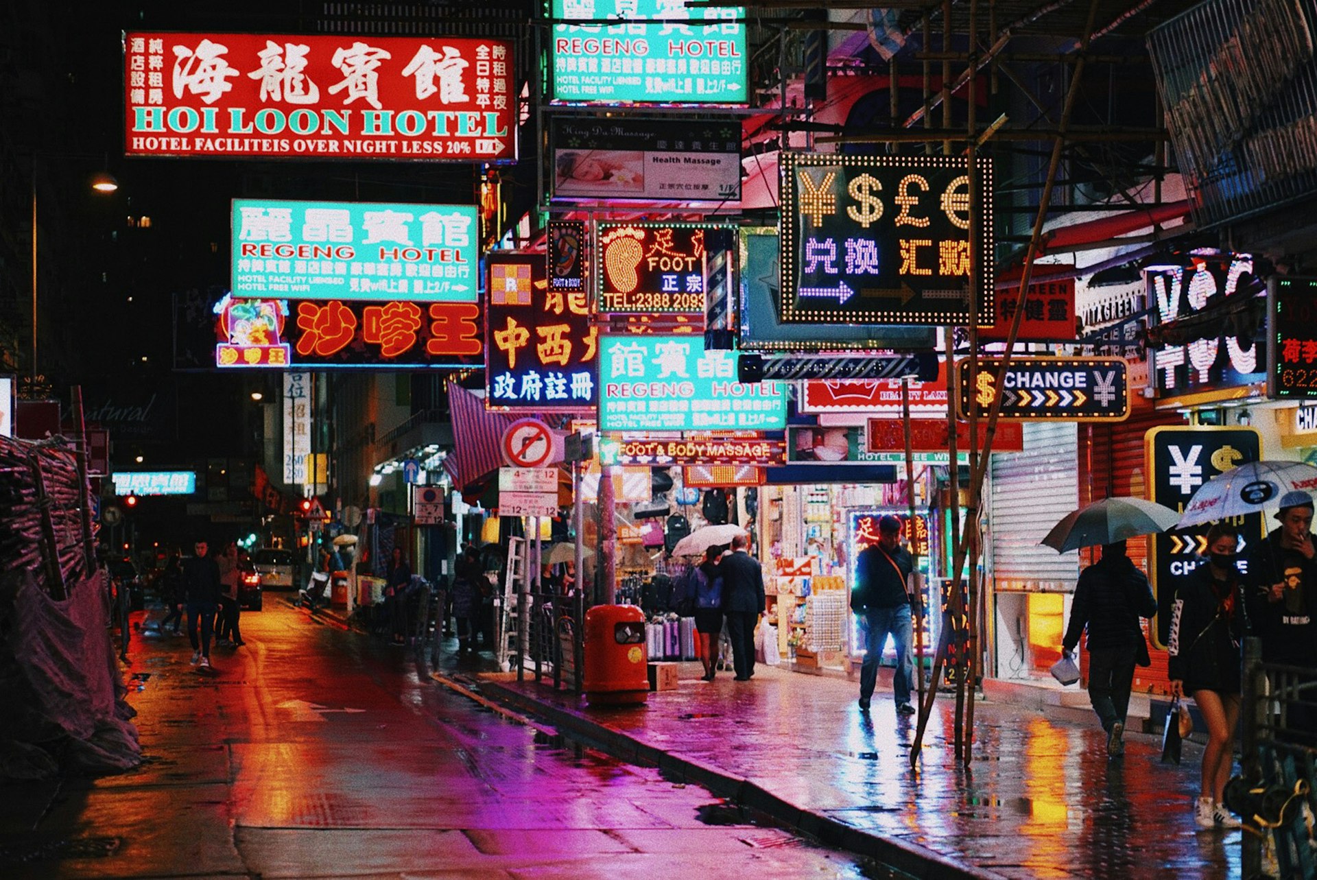 People walking on a wet city street under glowing neon signs in Hong Kong