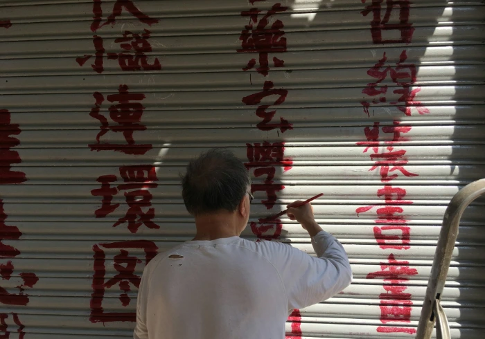 man painting Kanji text on roll-up door